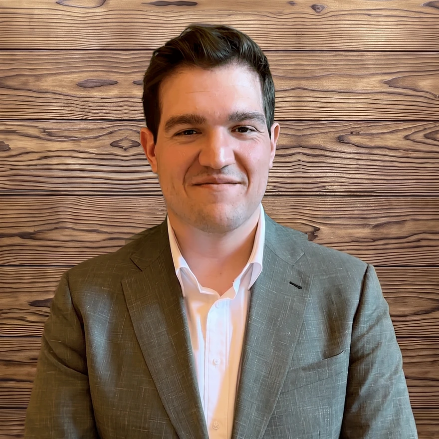 Jason Cruz, founder of Cruz Law, in a sage green suit against a charred wood plank wall
